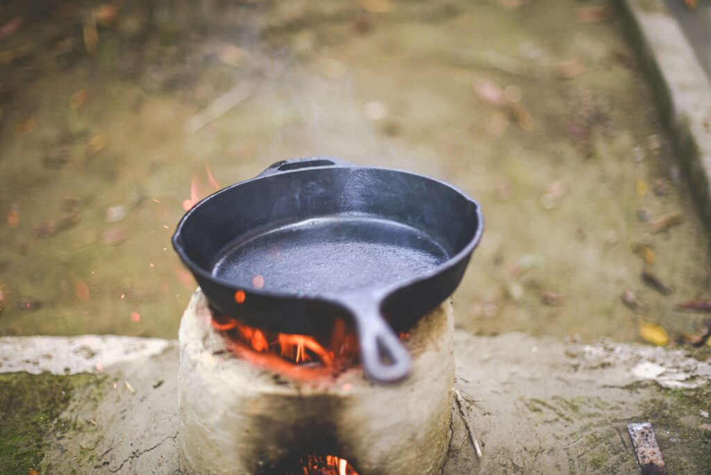 a cast iron pans and pots is reedy to cook to food ,heating over an open flame with sparks rising, set against a blurred natural background."