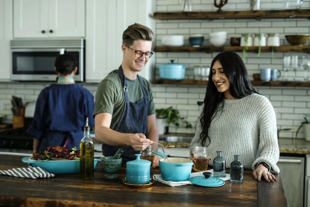 A couple cooking together in a smart kitchen with a variety of kitchen utensils and a blue cooking pot.