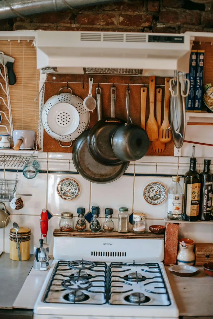 A rustic kitchen setup featuring cast iron pans, wooden utensils, and a variety of spices on a stove."